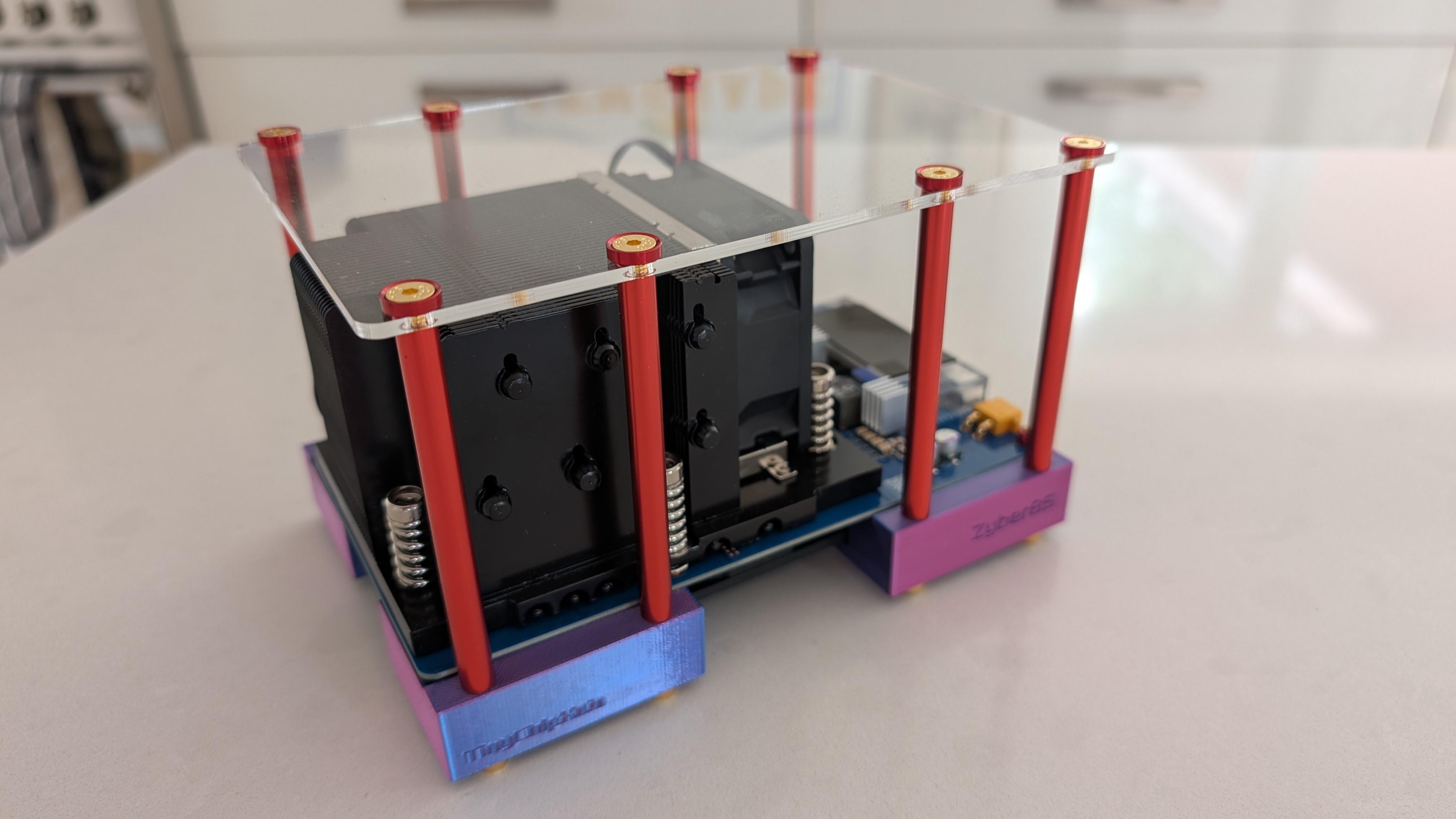 A Bitaxe-family solo miner in an open acrylic frame with tower heatsink, red standoffs and 3D-printed feet